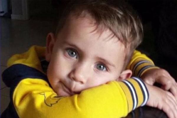 Child with blue eyes resting his head on his arms, wearing a yellow and navy hoodie.