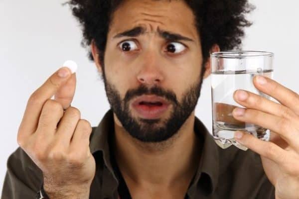 Man holding pill and glass of water, looking confused about contraception options.