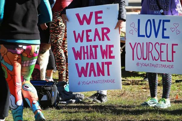 Women holding signs advocating for comfort and confidence in yoga pants.