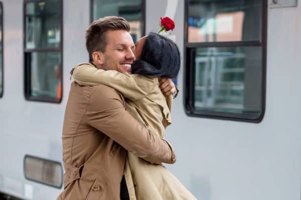 Happy couple embracing at train station, celebrating reunion after time apart.