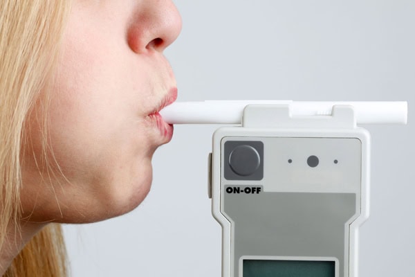 Woman using a breathalyser to check alcohol level before driving during school run.