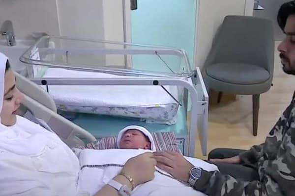 Mother and newborn in hospital bed, father holding baby's hand after birth.