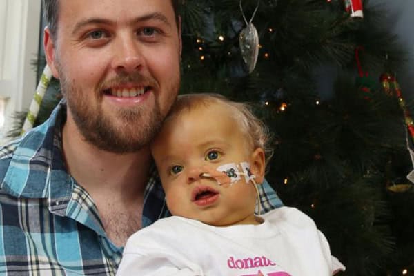 Father giving Christmas gift to son with Biliary Atresia in front of decorated tree.
