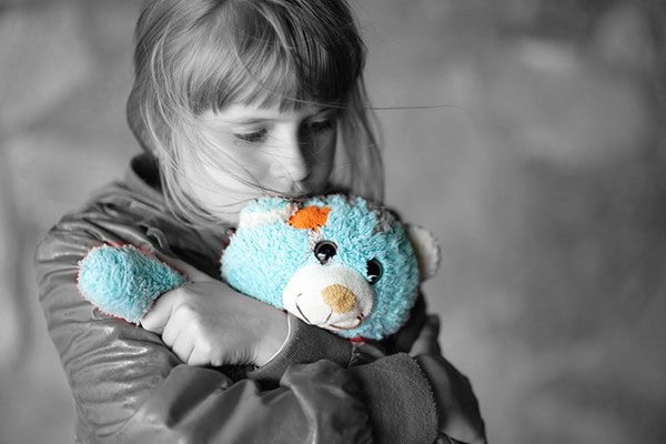 Child hugging a teddy bear, showing comfort during friendship loss.