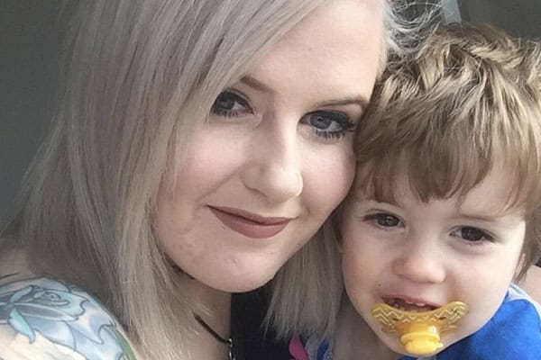 Young mum with blonde hair and her toddler with a pacifier, smiling together.