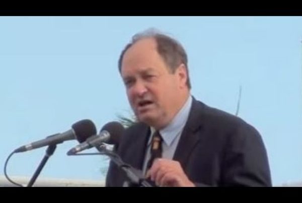 Controversial politician speaking at a public event, addressing a crowd with microphones.