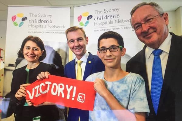 Teenager holding a victory banner with hospital officials after petition success.