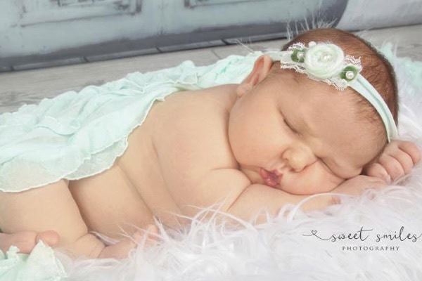 Baby girl sleeping peacefully on soft blanket with floral headband.