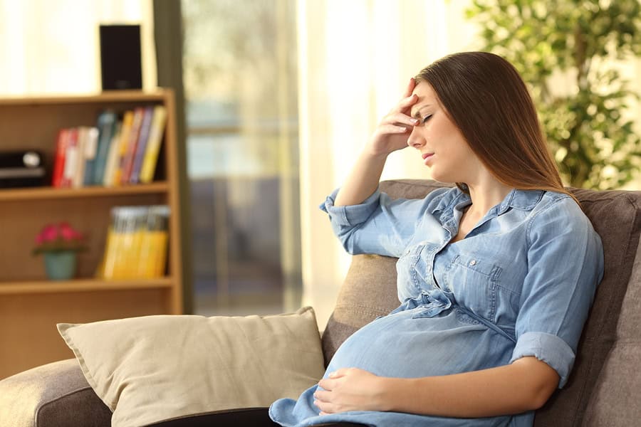 Pregnant woman experiencing discomfort at home, holding her head.