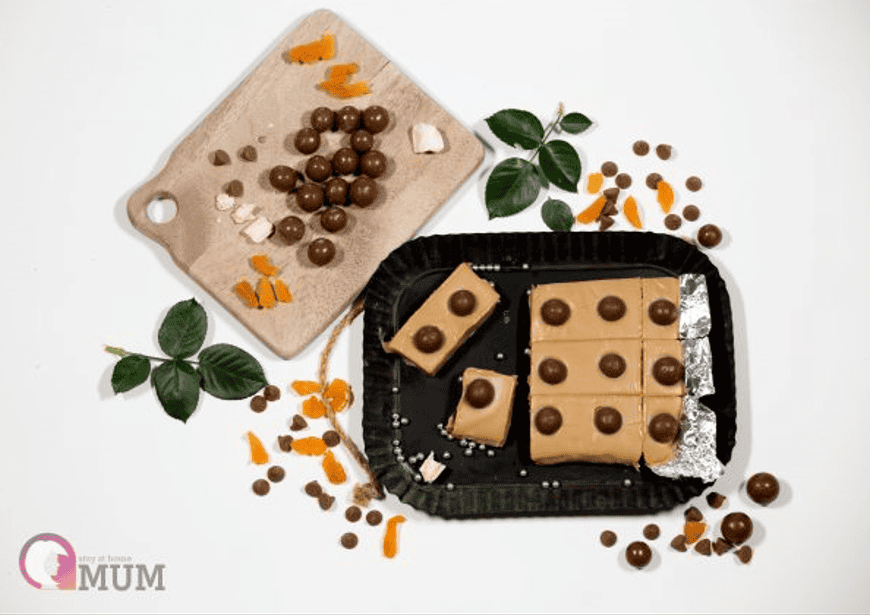 Delicious Malteser caramel and white chocolate fudge on a black tray with scattered ingredients.