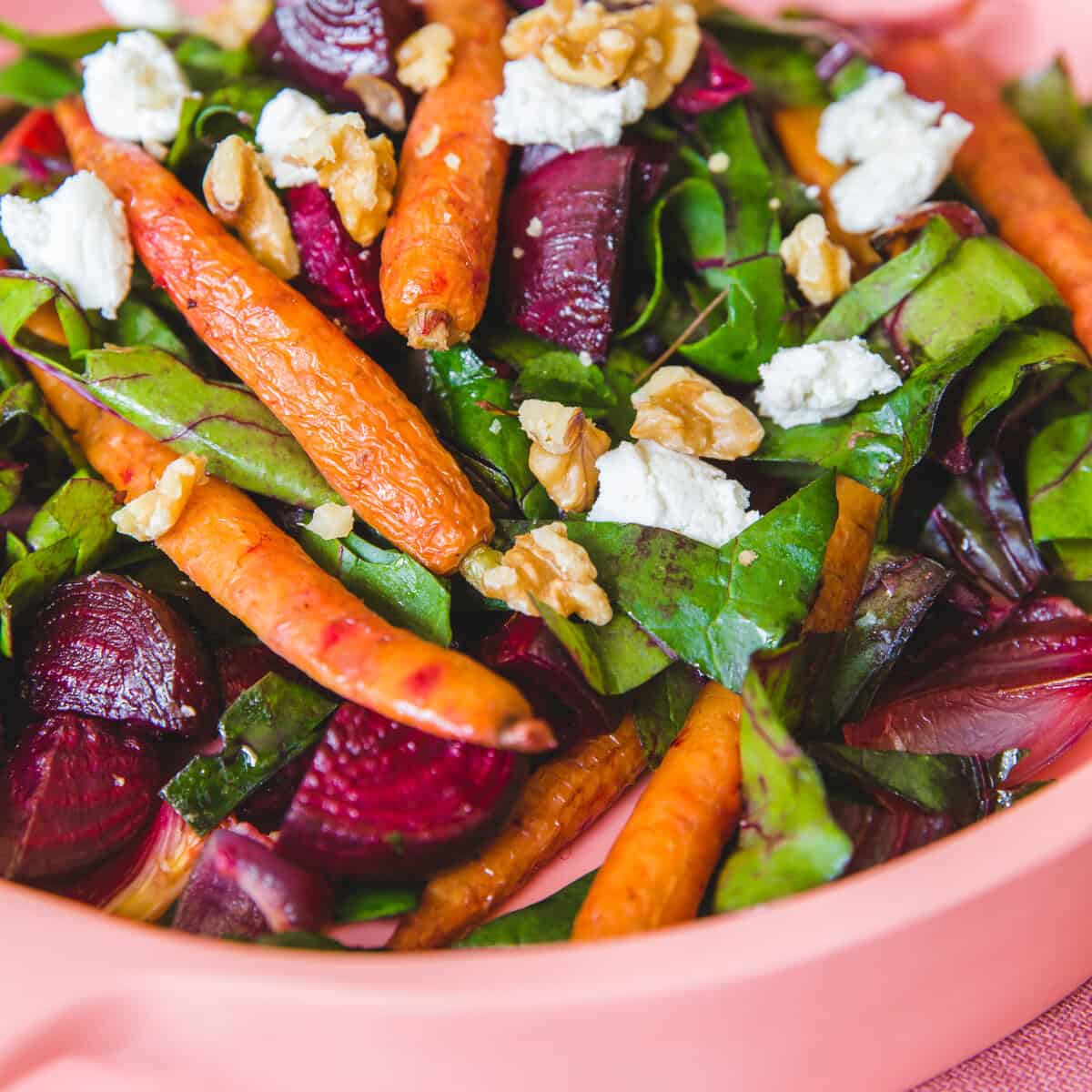 Fresh beetroot, lentil, and carrot salad with feta and walnuts in a pink bowl.