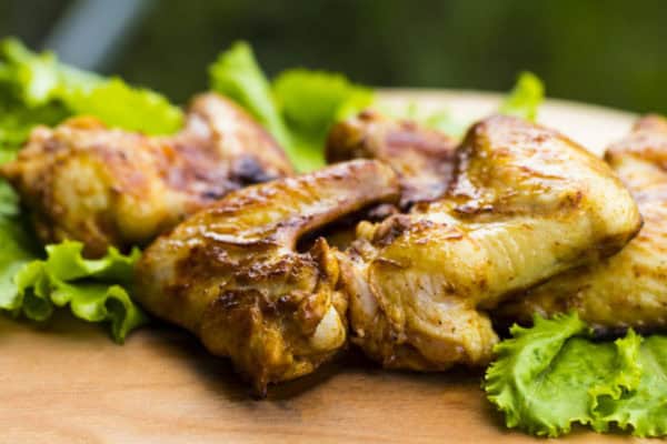 Chicken pieces on a wooden board with fresh greens.