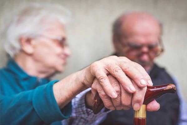 Elderly woman helping man with walking cane, highlighting early signs of dementia.