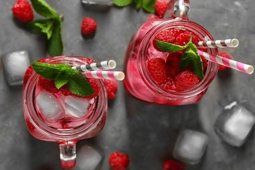 Raspberry Mojito with fresh raspberries, mint, and ice in glass jars.
