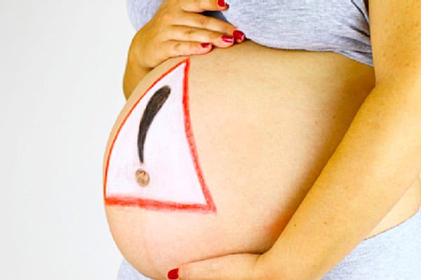 Pregnant woman with warning sign on belly highlighting unusual pregnancy complications.