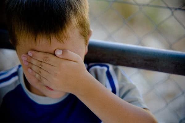 Child covering face with hand, feeling upset or distressed.