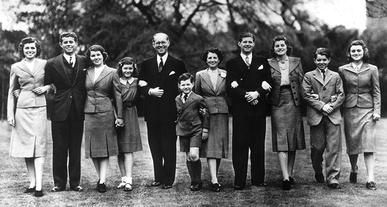 Family portrait of children and adults in formal attire, representing wealthy family heritage.