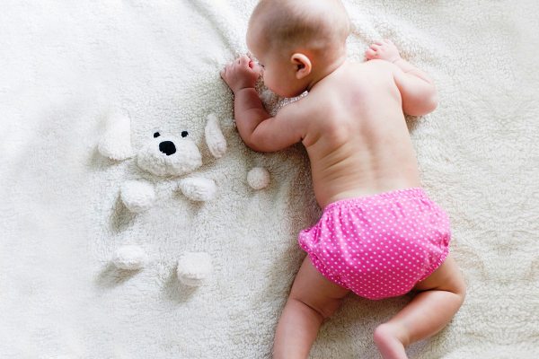 Baby girl sleeping on a soft blanket with a teddy bear, wearing pink polka dot diaper.