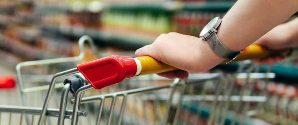 Close-up of a hand holding a shopping cart handle at a supermarket.