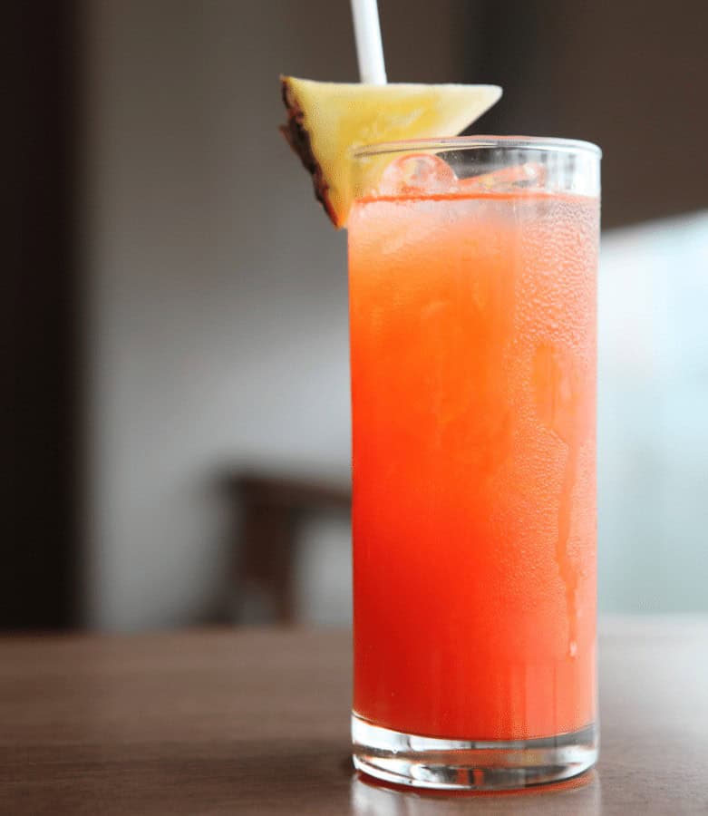 Bright tropical punch with pineapple garnish in a tall glass.