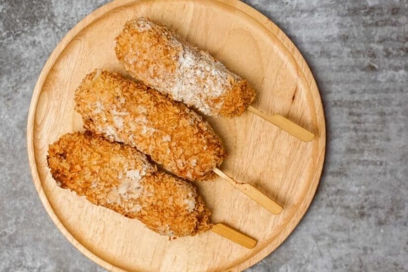 Crispy fish fingers with golden coating served on a round wooden plate, perfect for a family snack o.