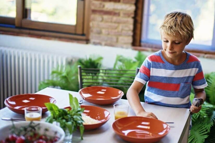 Child setting a dinner table with plates and utensils.