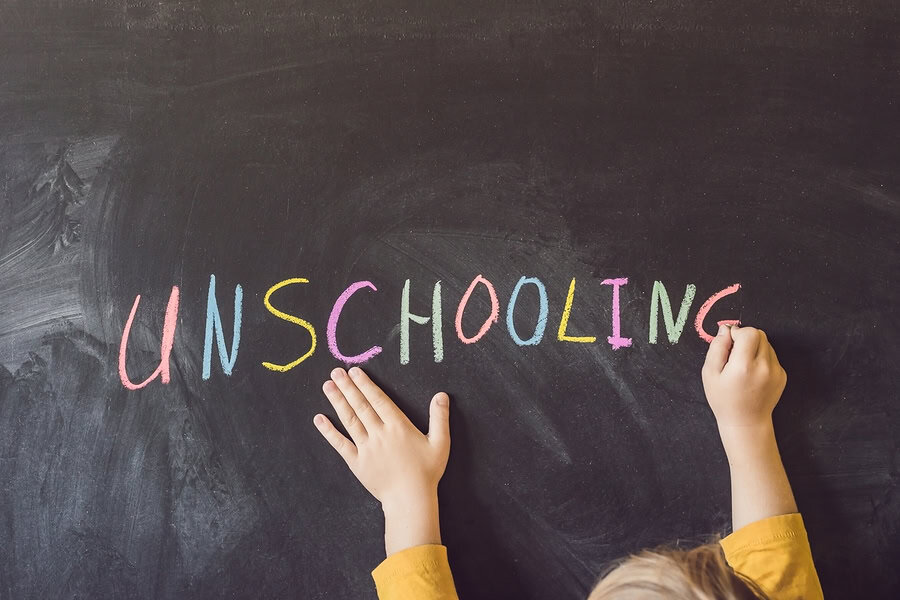 Child writing "Unschooling" on blackboard, promoting alternative education methods.