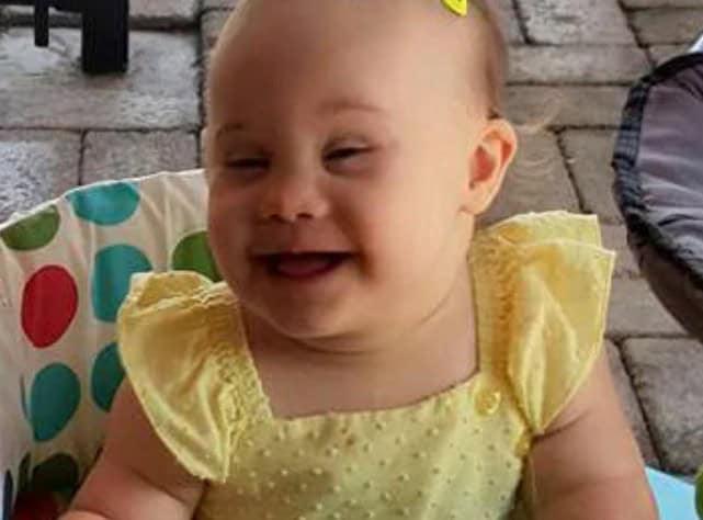 Child in yellow dress smiling outdoors.