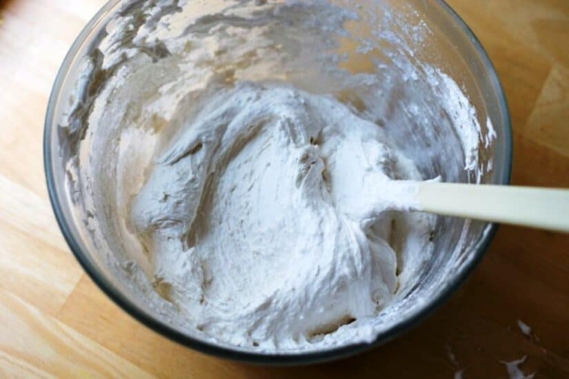 Bowl of white puff paint mixture with a spatula on a wooden surface.