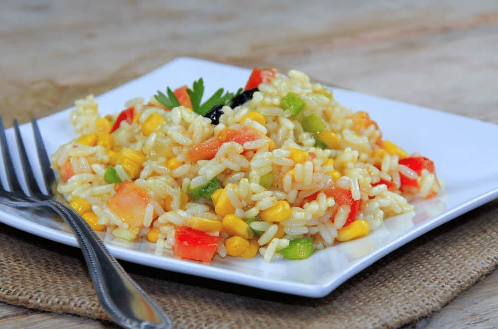 Cold rice salad with vegetables on a white plate, fresh and colorful.