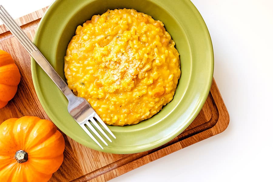 Delicious creamy pumpkin risotto served in a green bowl with pumpkins around.