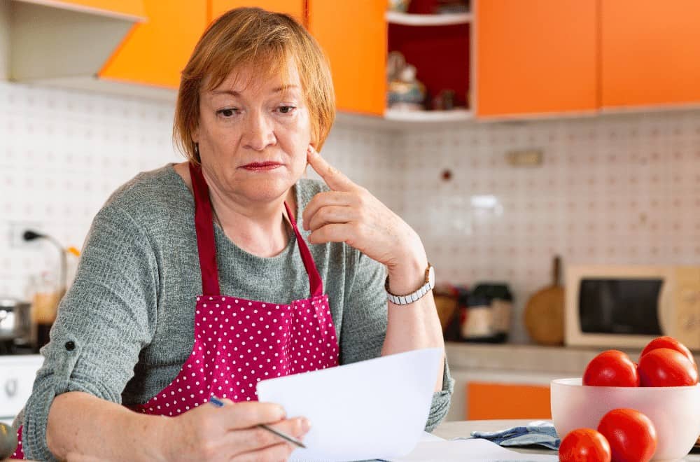 Woman thinking about grocery shopping on a budget in the kitchen.
