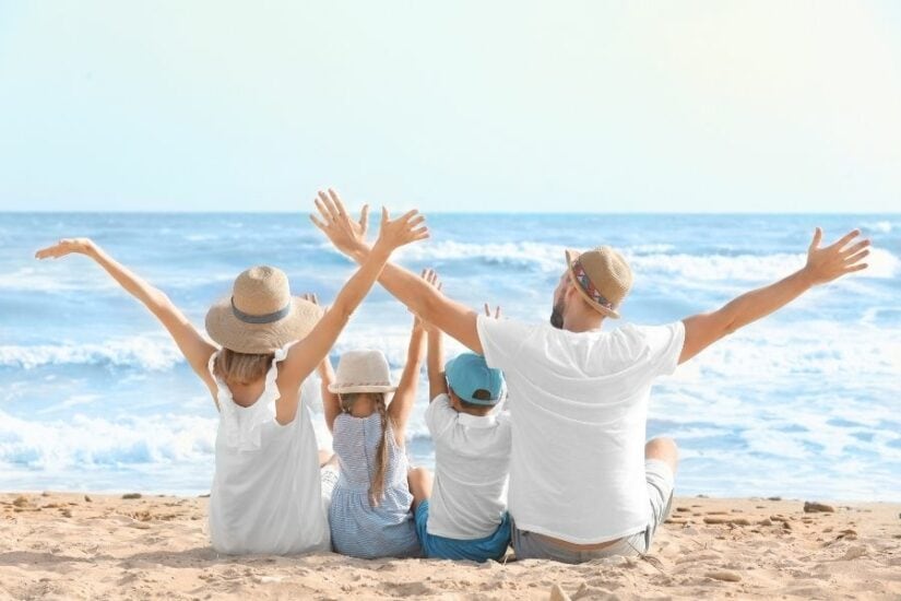 Family relaxing on the beach with arms raised, enjoying the ocean view.