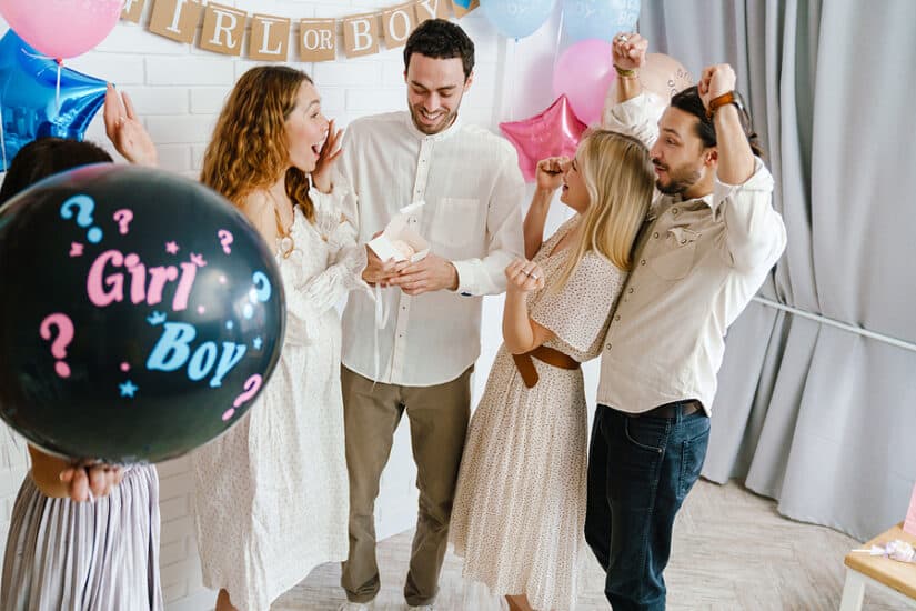 Group of friends celebrating a gender reveal with balloons and gifts at a party.