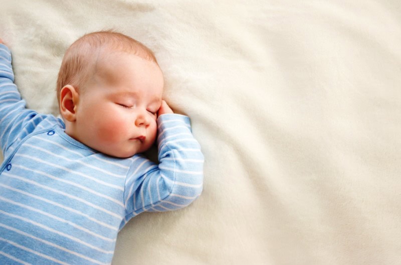 Baby sleeping peacefully on a bed in a blue striped outfit.