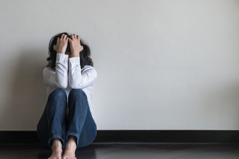 Woman sitting on the floor with hands on her head, feeling overwhelmed and anxious.