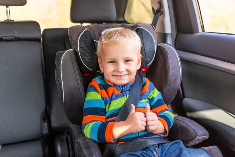 Child in booster seat with a big smile, secured in a safe car seat for kids.
