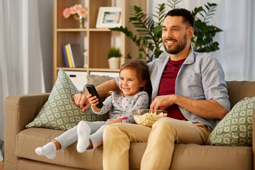 Family enjoying TV together with a young girl holding a remote control.