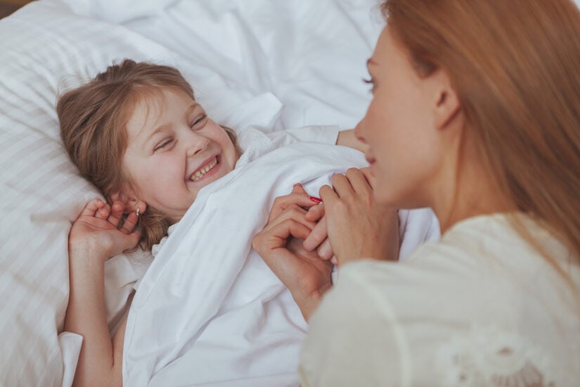 Child and mother talking happily in bed during bedtime.
