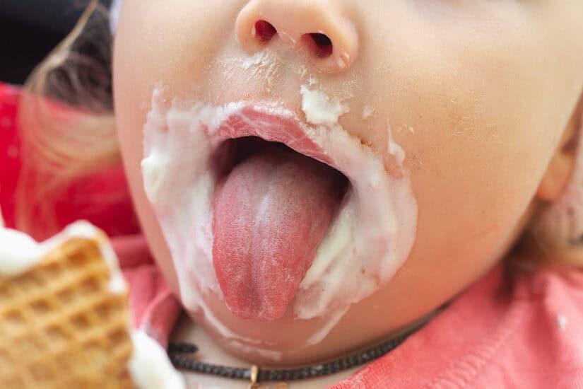 Baby enjoying breast milk ice cream with a messy face and tongue out.