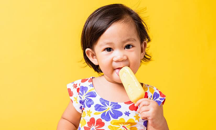 Baby eating breast milk ice cream on a yellow background.