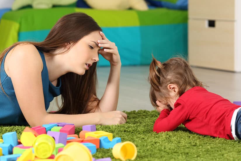 Frustrated mother and toddler playing with toys on the floor.