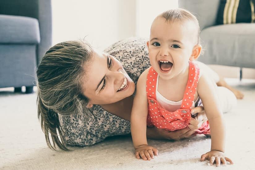 Happy mother and toddler playing on the floor at home.