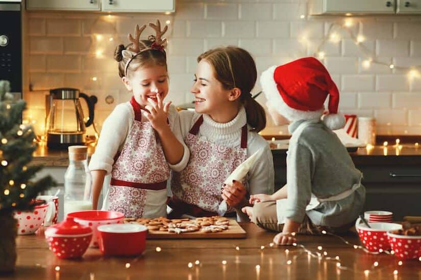 Family baking Christmas cookies in a decorated kitchen with holiday lights.