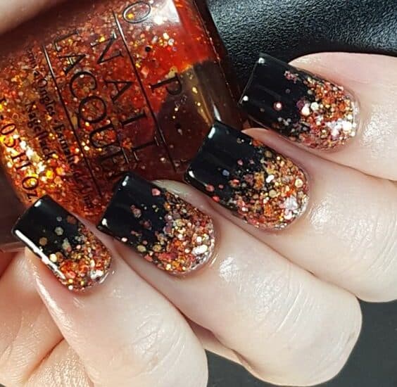 Beautiful Halloween-themed nails featuring black polish with orange, gold, and silver glitter accent.