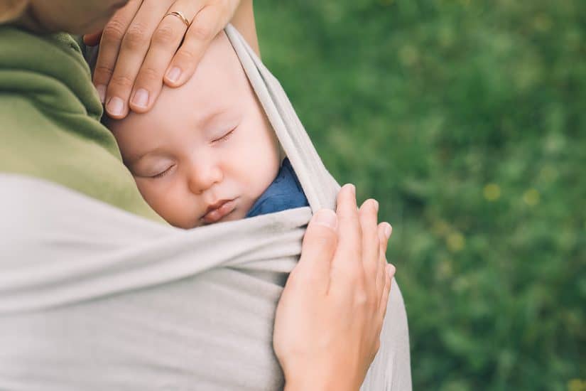 Baby sleeping peacefully in a wrap carrier outdoors.