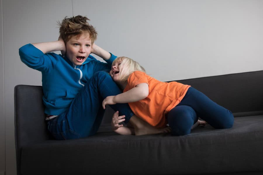 Two kids arguing and fighting on a sofa during school holidays.