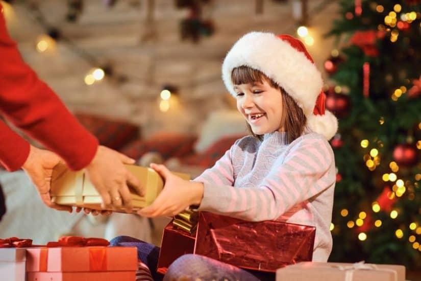 Christmas gift exchange with a young girl in a Santa hat receiving a present.