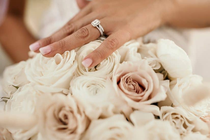 Elegant wedding ring on finger resting on a bouquet of roses.