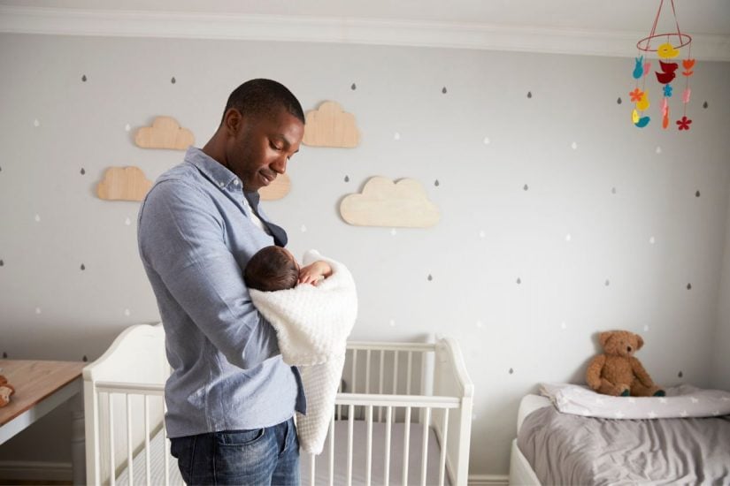 Father holding newborn baby in nursery, bonding with infant.